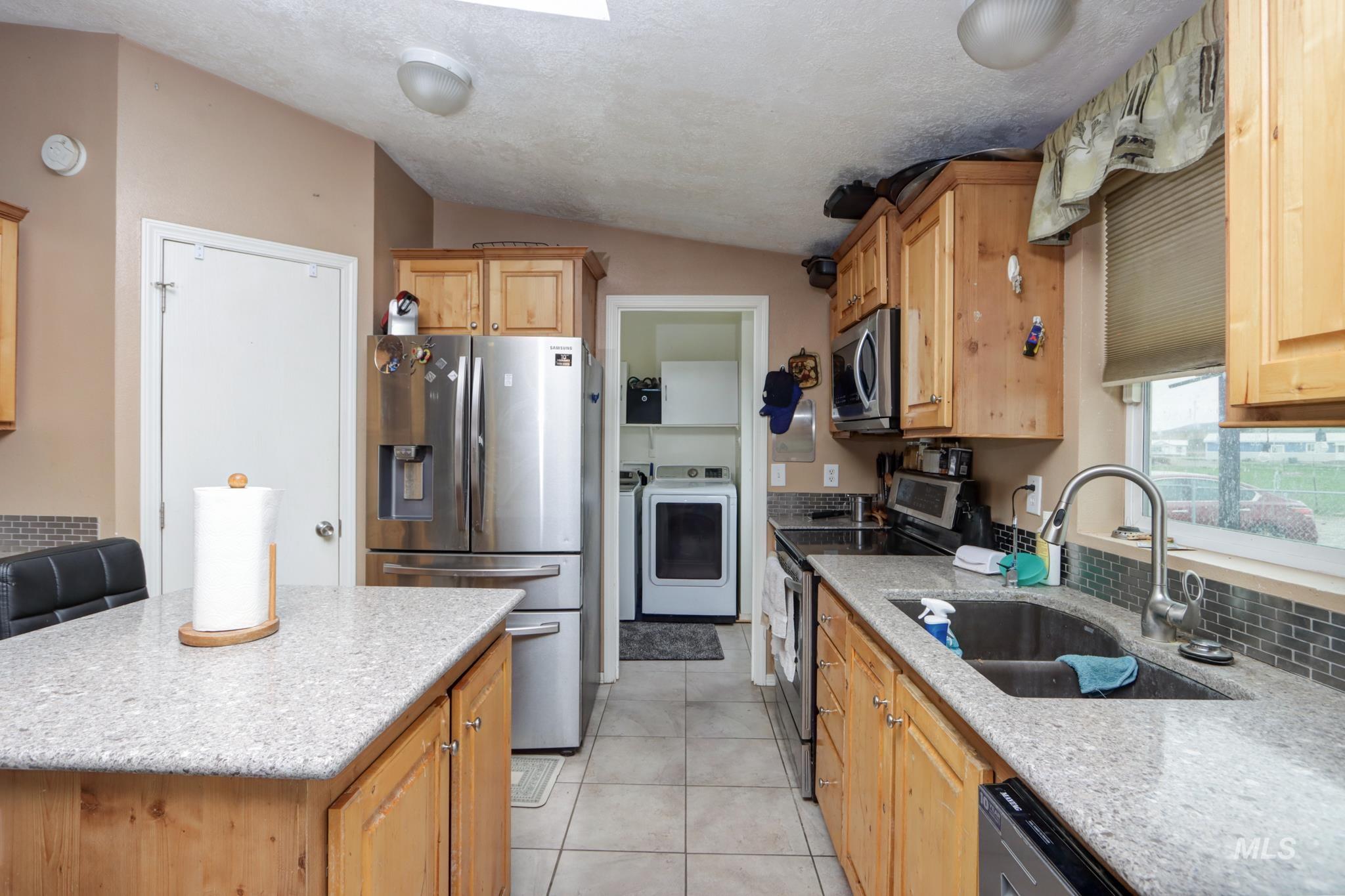 1583 Dustin Lane Vale, OR 97918 - Photo 5 of 39 Kitchen with stainless steel appliances, light stone counters, light wood finish cabinetry, light tile patterned flooring, and a center island