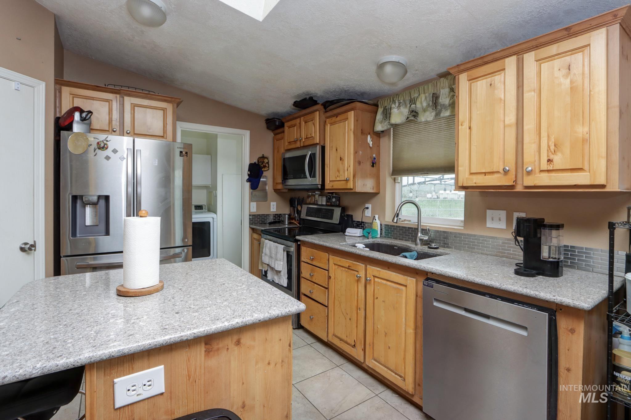 1583 Dustin Lane Vale, OR 97918 - Photo 6 of 39 Kitchen featuring stainless steel appliances, light stone counters, washer / clothes dryer, light tile patterned floors, and a skylight