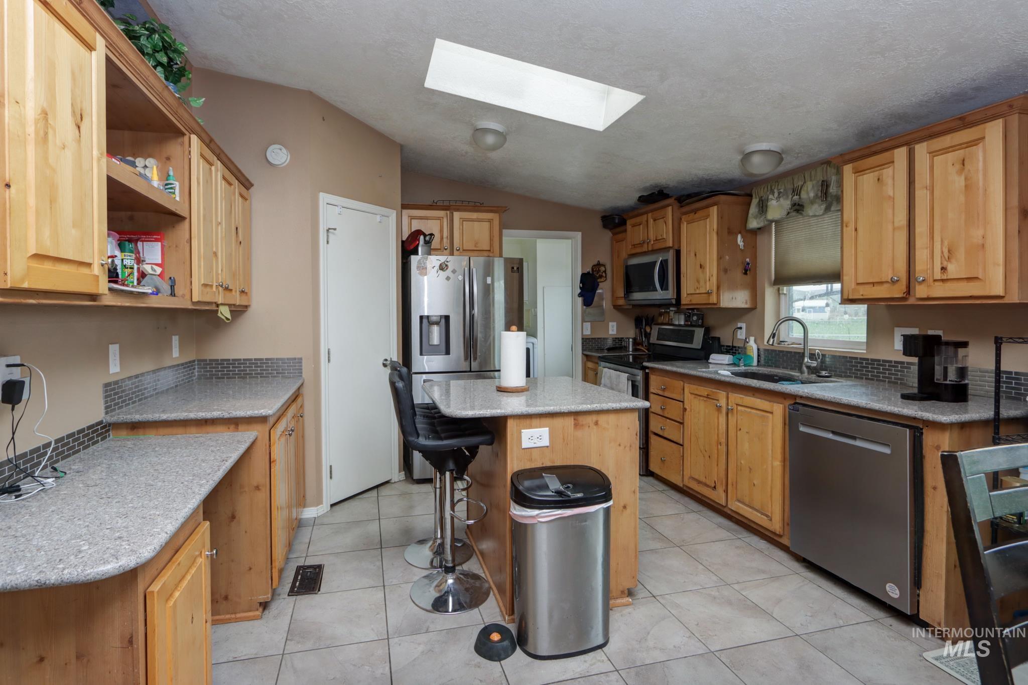 1583 Dustin Lane Vale, OR 97918 - Photo 7 of 39 Kitchen featuring a skylight, stainless steel appliances, a center island, a kitchen bar, and light stone countertops