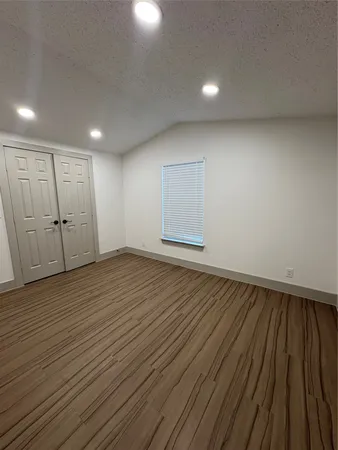 an empty room with wooden floor closet and windows