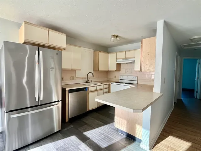 a kitchen with stainless steel appliances granite countertop a refrigerator a sink dishwasher a stove and white countertops with wooden floor