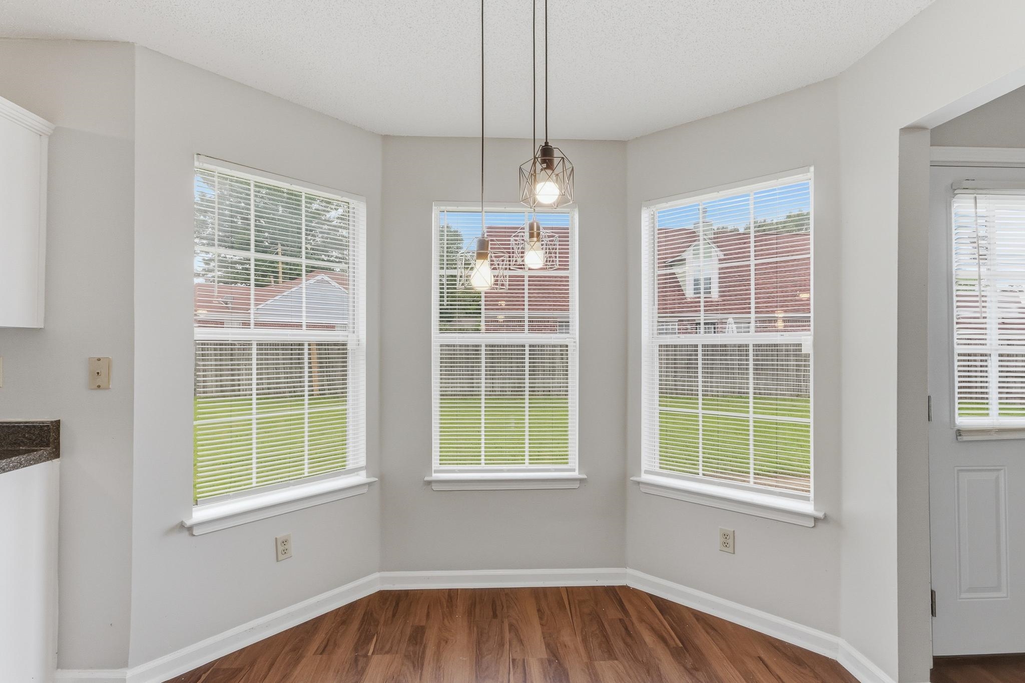 4101 Long Creek Road Memphis, TN 38125 - Photo 13 of 36 Bay window area featuring three large windows with white blinds, wood-finish flooring, and two modern pendant light fixtures