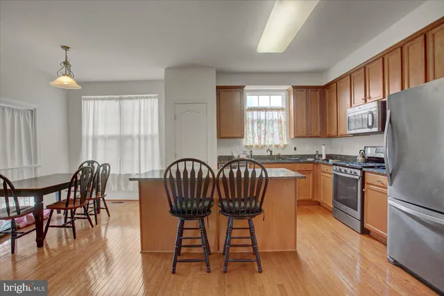 a kitchen with granite countertop a dining table chairs a refrigerator a stove a sink with wooden floor and cabinets