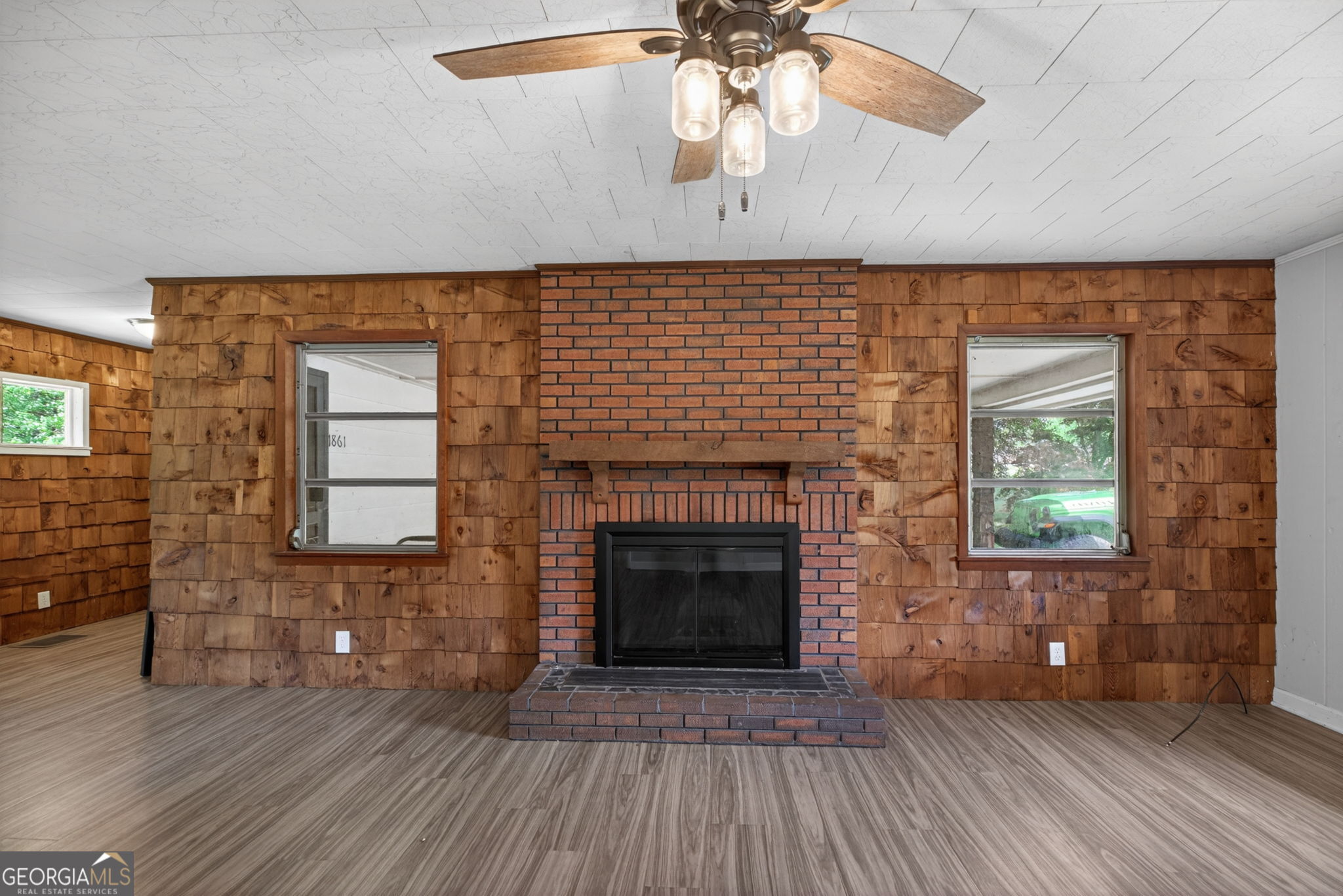 1861 Highway 100 Bowdon, GA 30108 - Photo 19 of 35 an empty room with wooden floor a fireplace a ceiling fan and windows