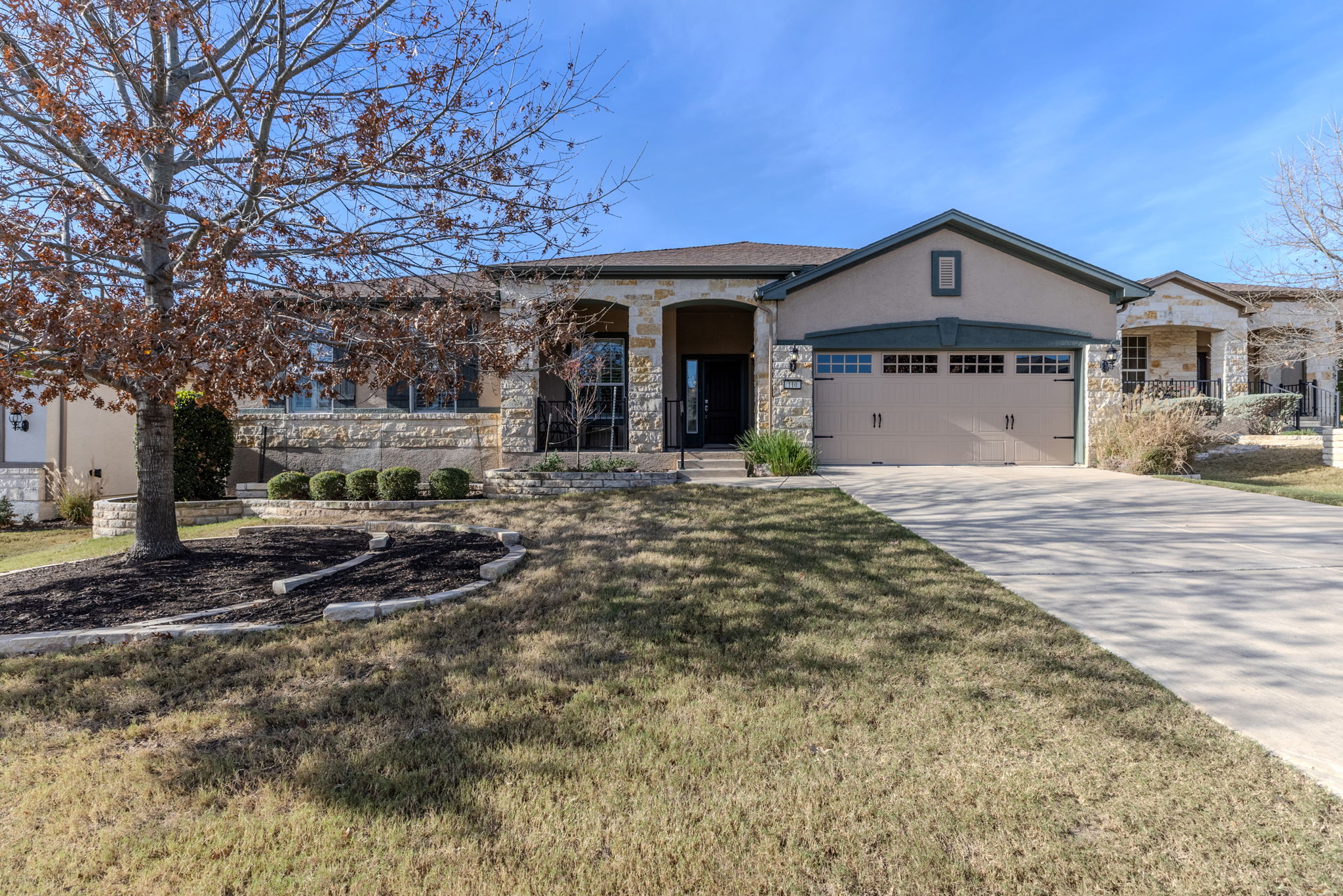 View of front facade with stone siding, driveway, a front lawn, stucco siding, and an attached garage