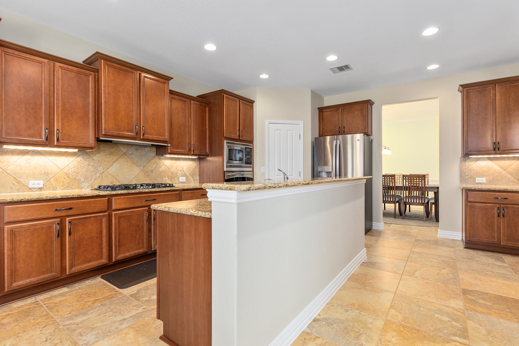 110 Emory Peak Trail Georgetown, TX 78633 - Photo 15 of 39 Kitchen with tasteful backsplash, brown cabinets, stainless steel appliances, light stone countertops, and a center island with sink