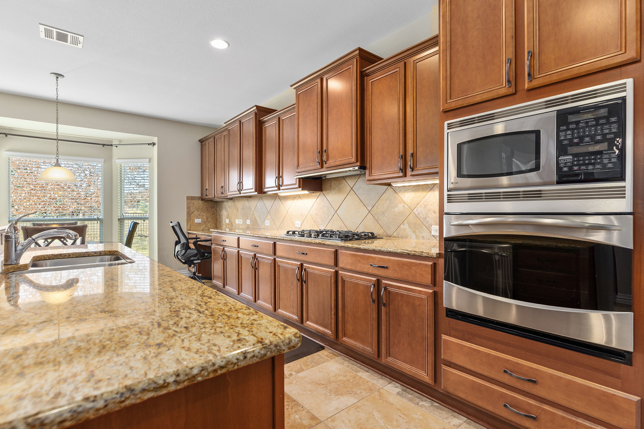 110 Emory Peak Trail Georgetown, TX 78633 - Photo 18 of 39 Kitchen with appliances with stainless steel finishes, brown cabinetry, light stone countertops, pendant lighting, and recessed lighting