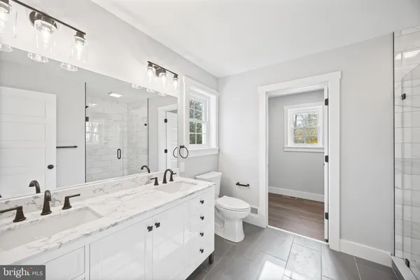 a bathroom with a granite countertop double vanity sink a mirror and a shower
