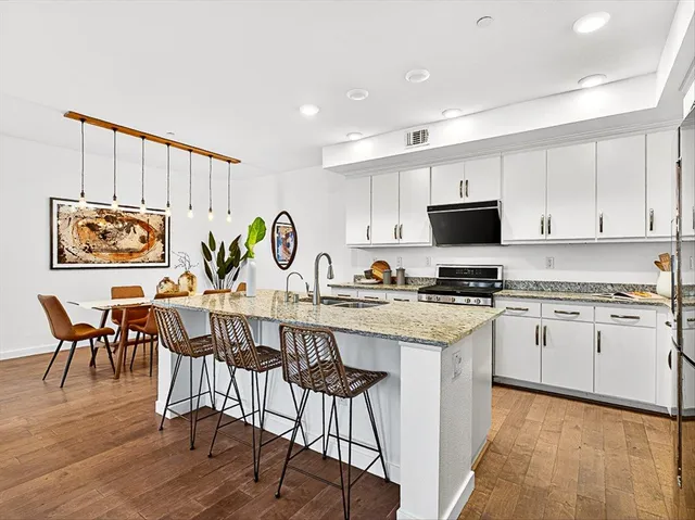 a kitchen with stainless steel appliances granite countertop a stove top oven a sink a refrigerator with a dining table and chairs with wooden floor