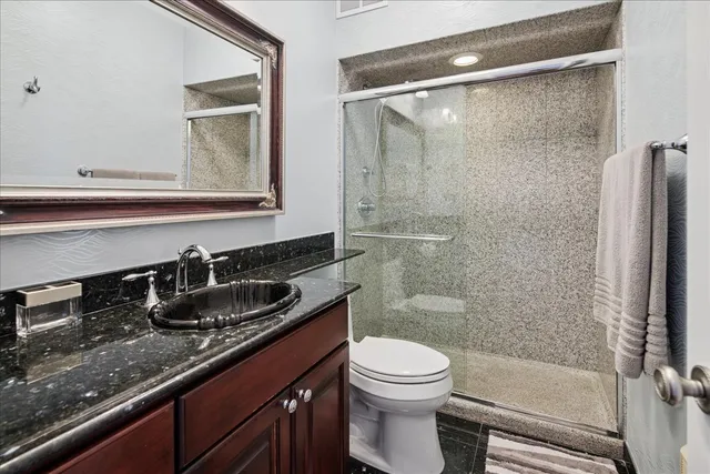 a bathroom with a granite countertop sink a toilet a mirror and shower