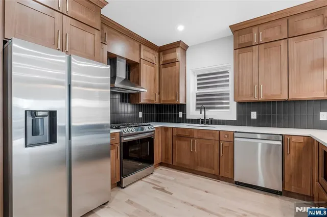 a kitchen with stainless steel appliances granite countertop a refrigerator a stove and a sink with wooden floor