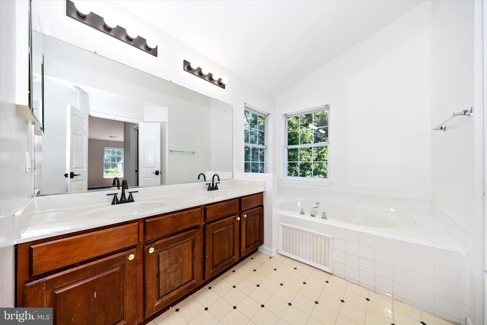 803 Apache Court Frederick, MD 21701 - Photo 19 of 46 a bathroom with a double vanity sink a large mirror a bathtub and window
