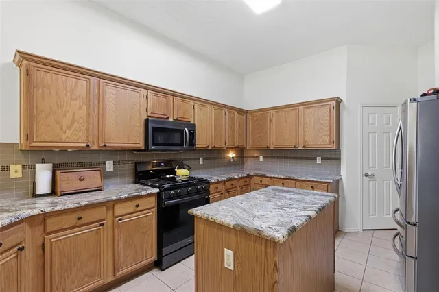 a kitchen with stainless steel appliances granite countertop a stove top oven a sink dishwasher and a refrigerator with wooden cabinets