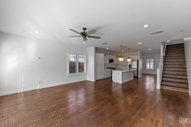 a view of an empty room with wooden floor and a kitchen
