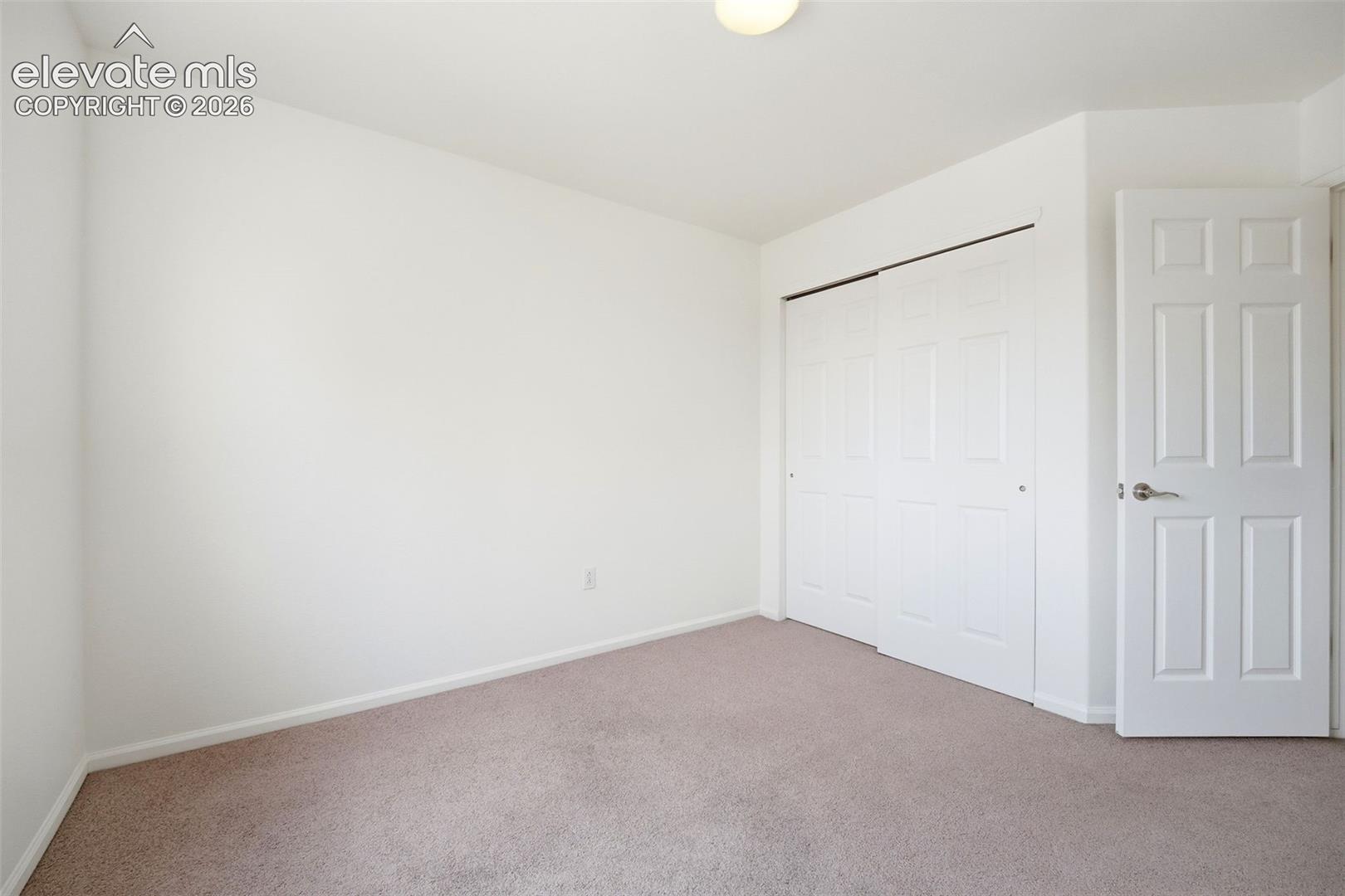 7904 Coffee Road Peyton, CO 80831 - Photo 26 of 48 Light-colored carpeting complementing white walls, featuring a bi-fold closet and a six-panel interior door with brushed nickel hardware