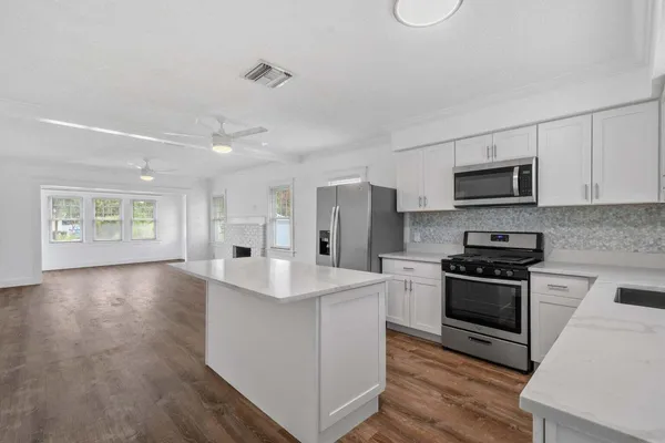 a kitchen with stainless steel appliances a stove top oven a sink dishwasher a refrigerator and white cabinets with wooden floor