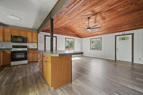 a kitchen with stainless steel appliances granite countertop a stove top oven a sink dishwasher a microwave oven and a dining table with wooden floor