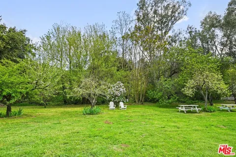 a view of a white house in a big yard with table and chairs under an umbrella