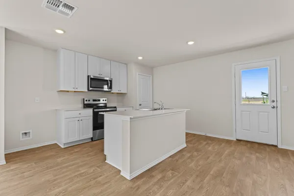 a view of kitchen with kitchen island a sink a stove a refrigerator and white cabinets