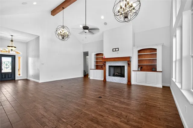 an empty space with a fireplace a ceiling fan and wooden floor