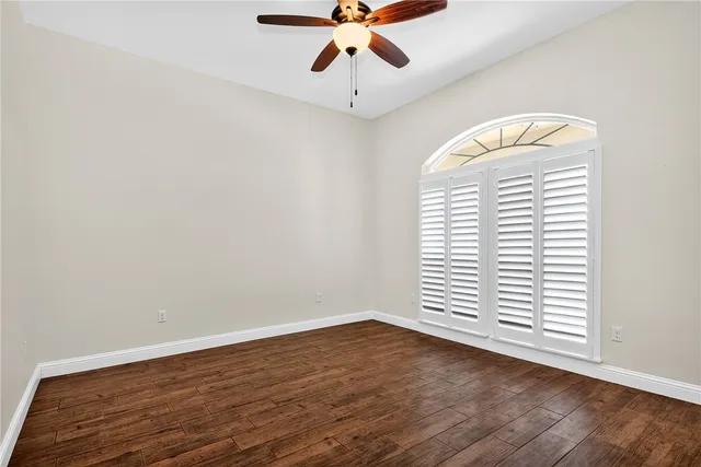 an empty room with wooden floor chandelier fan and windows