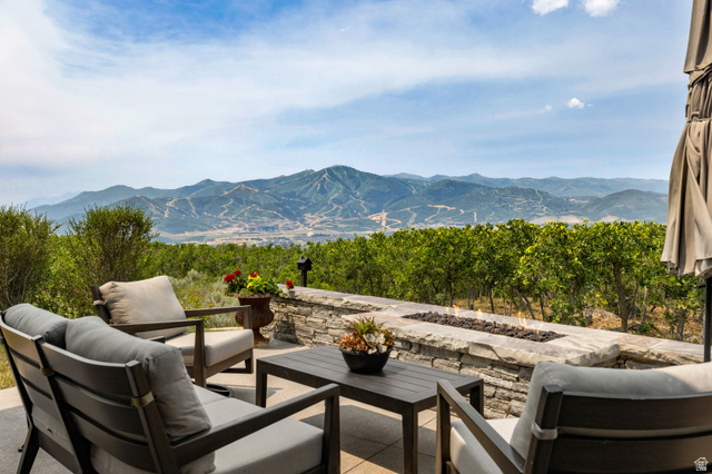 11547 Soaring Hawk Lane Hideout, UT 84036 - Photo 3 of 43 Expansive outdoor patio featuring a stone-clad fire pit, mature green foliage, a paved surface, and distant mountain scenery