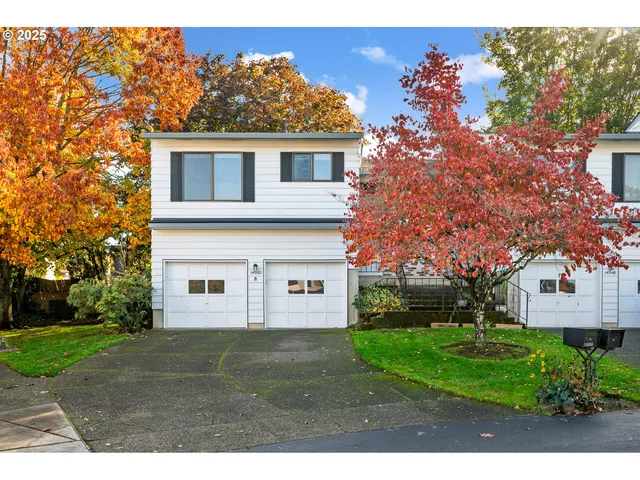 a view of a white house next to a yard with big trees