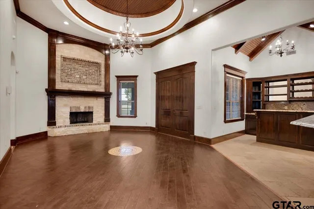 an empty room with wooden floor fireplace and chandelier