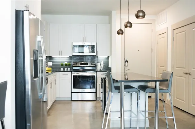 a kitchen with stainless steel appliances a refrigerator a stove and white cabinets