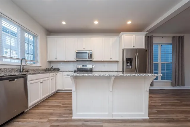 a kitchen with stainless steel appliances granite countertop a refrigerator a sink dishwasher a stove and white countertops with wooden floor