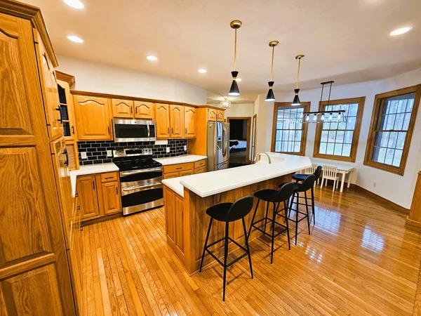 a kitchen with stainless steel appliances kitchen island granite countertop a stove top oven a sink a dining table and chairs with wooden floor