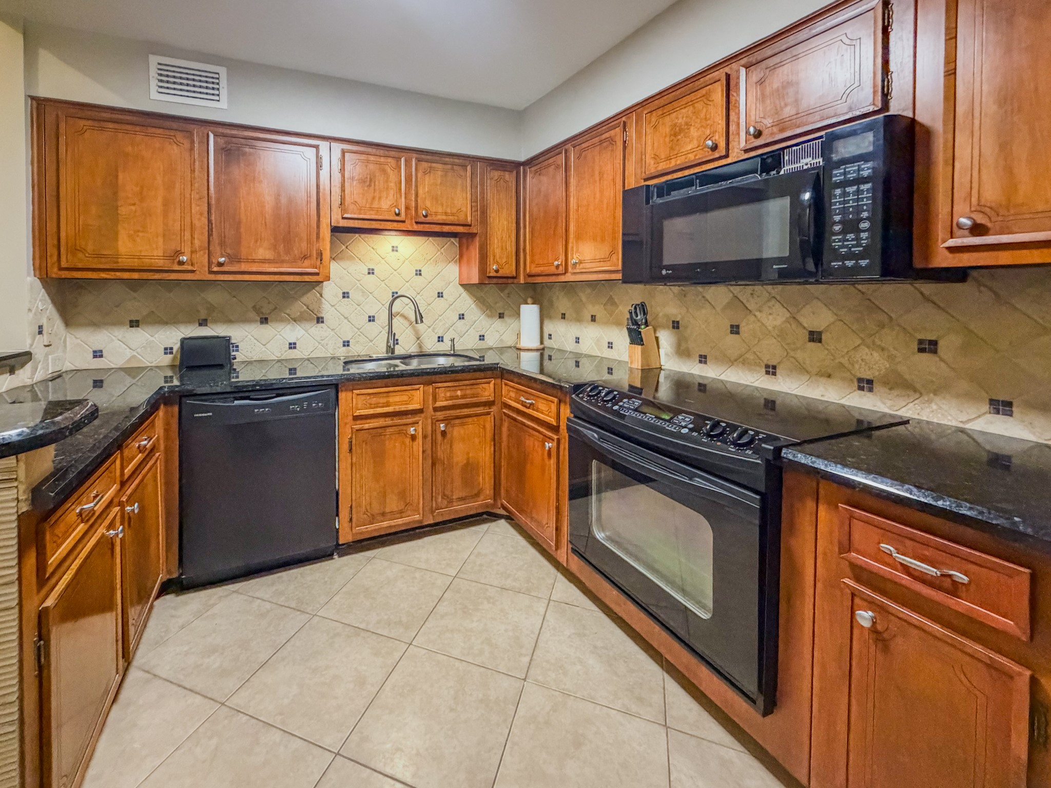 2574 Marilee Lane, Unit 23 Houston, TX 77057 - Photo 5 of 22 The kitchen highlights sleek black granite counters and matching appliances, fridge, plateware, & utensils