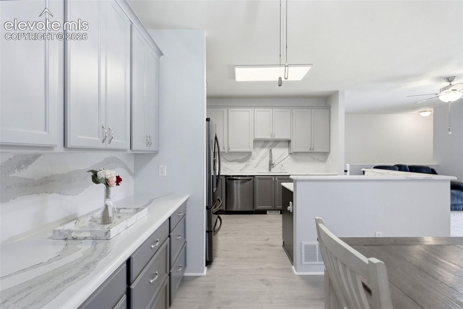 2002 Legacy Ridge View, Unit 107 Colorado Springs, CO 80910 - Photo 9 of 25 White shaker-style upper cabinetry with stainless steel hardware, gray lower cabinetry, light wood-finish flooring, and white countertops with integrated backsplash