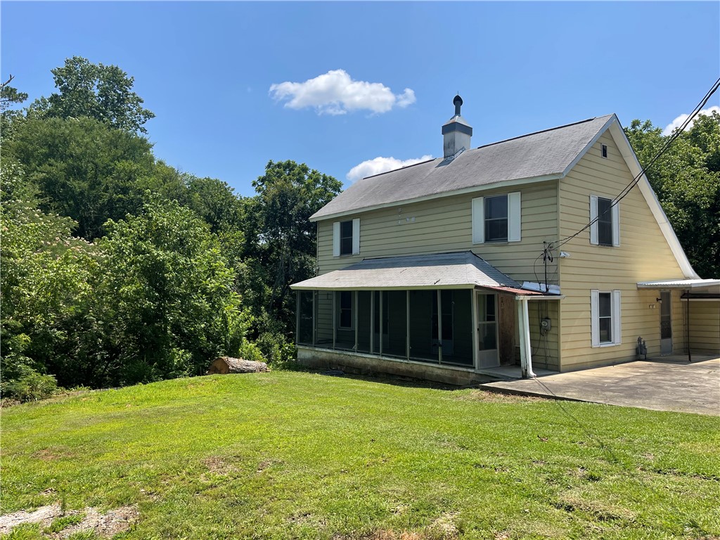 A classic two-story home features a screened-in porch and an attached carport, nestled among mature trees.