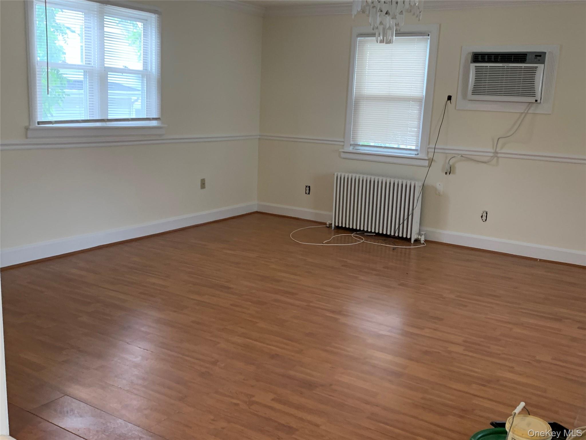 7 Clinton Street Haverstraw, NY 10927 - Photo 4 of 20 Spacious room featuring wood-finish flooring, two large windows with blinds, a wall-mounted air conditioning unit, and a decorative chandelier