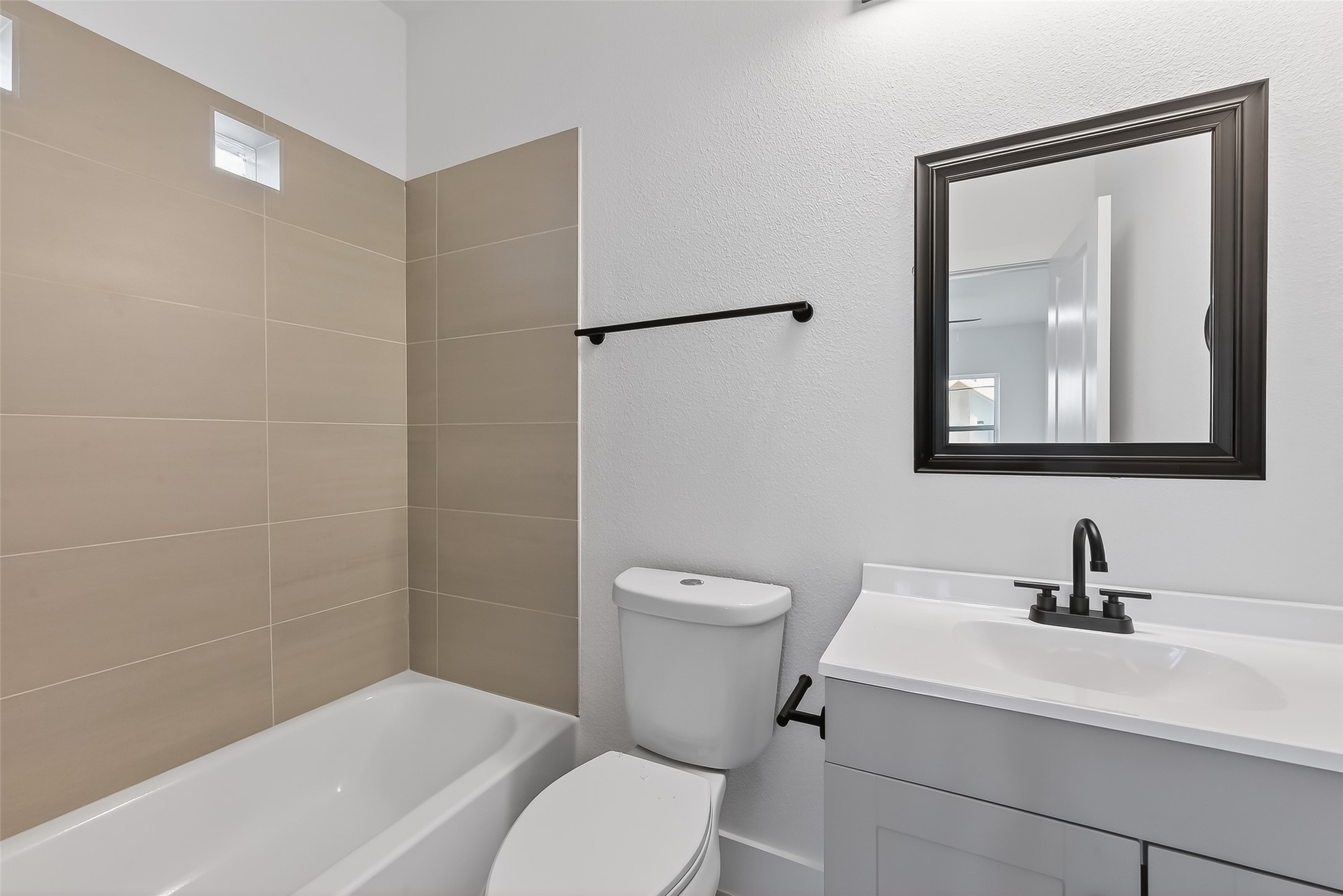 3514 Good Hope Street, Unit B Houston, TX 77021 - Photo 18 of 26 This bathroom features a modern design with neutral beige tiles in the shower area, a sleek white vanity, and a black framed mirror. The fixtures are contemporary, and the space is well-lit, providing a clean and inviting atmosphere.