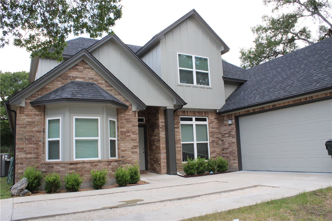 a view of a brick house with a yard plants and large tree