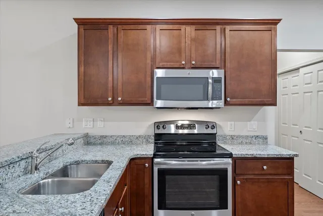 a kitchen with stainless steel appliances granite countertop wooden cabinets a refrigerator a stove a sink and a fireplace