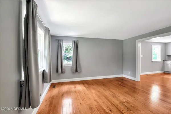 a view of empty room with kitchen view and wooden floor