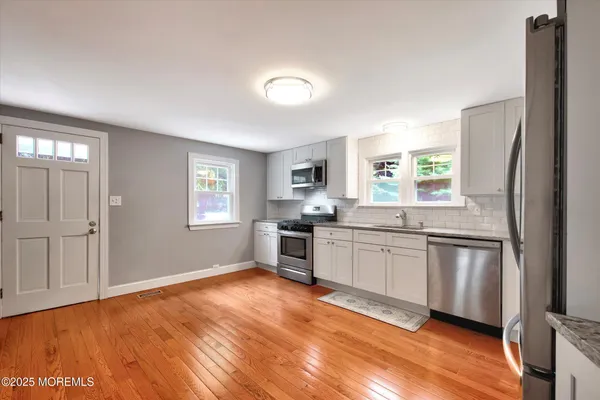 a kitchen with stainless steel appliances granite countertop white cabinets a sink dishwasher and a stove with wooden floor