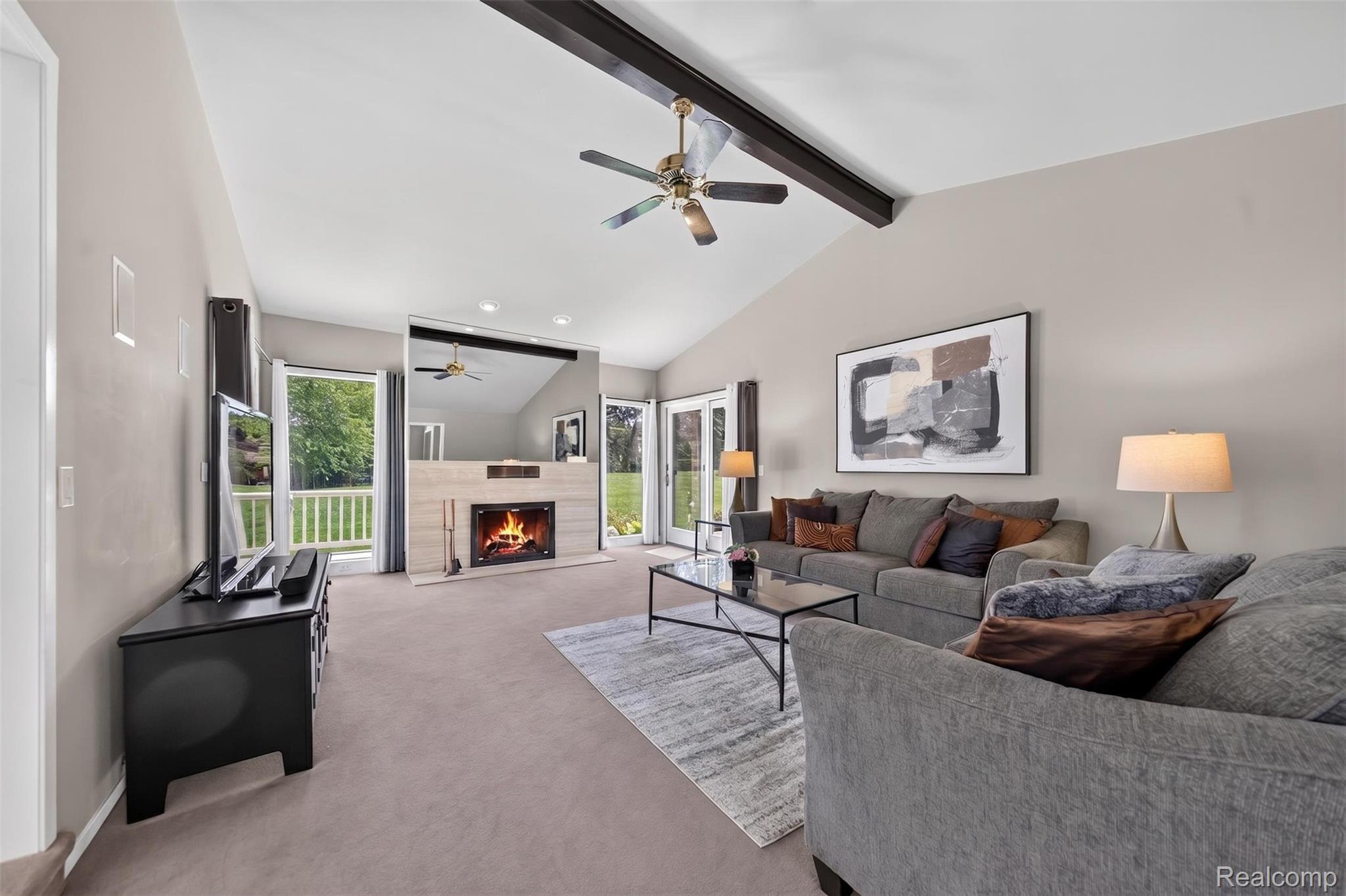 1236 Chaffer Drive Rochester, MI 48306 - Photo 7 of 76 Vaulted ceiling living room featuring a fireplace with a light-toned surround, a ceiling fan, and exposed dark-stained beams