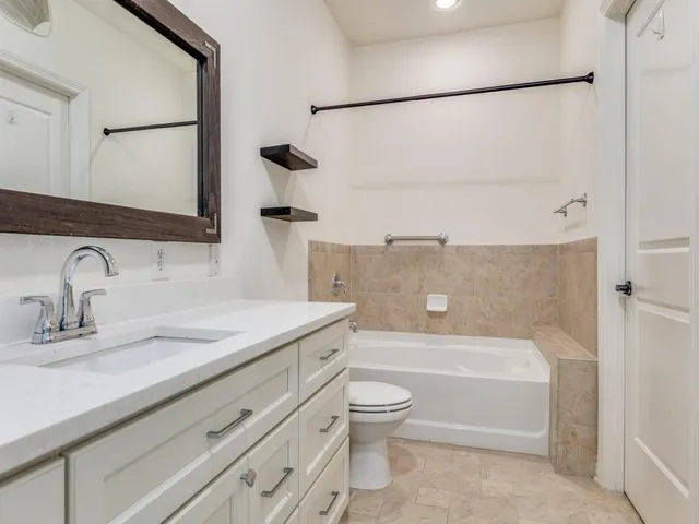 a bathroom with a granite countertop bathtub shower sink vanity and toilet