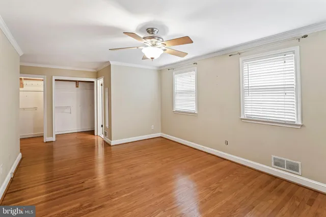 an empty room with wooden floor fan and windows