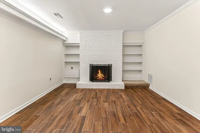 a view of an empty room with wooden floor fireplace and a window