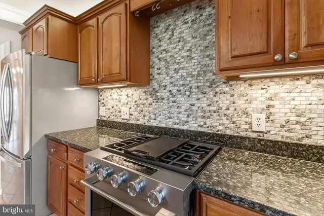 a kitchen with stainless steel appliances granite countertop a stove top oven a refrigerator a dining table and chairs with wooden floor