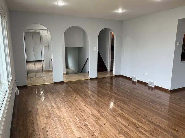 a view of an empty room with wooden floor and a ceiling fan