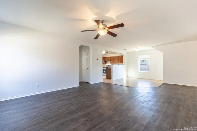 a view of an empty room with wooden floor and a ceiling fan