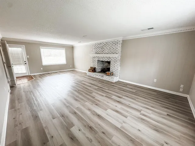 an empty room with wooden floor fireplace and windows