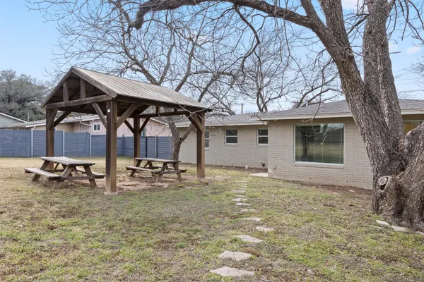 a backyard of a house with table and chairs under an large tree