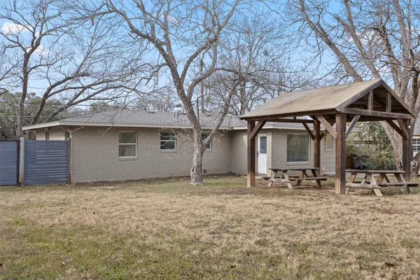 a backyard of a house with large trees and table and chairs
